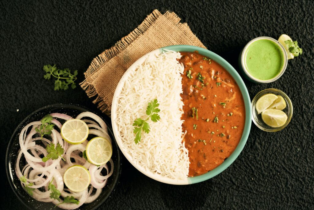 Top view of Indian curry with rice, green sauce, onions, and lime slices in a flat lay arrangement.
