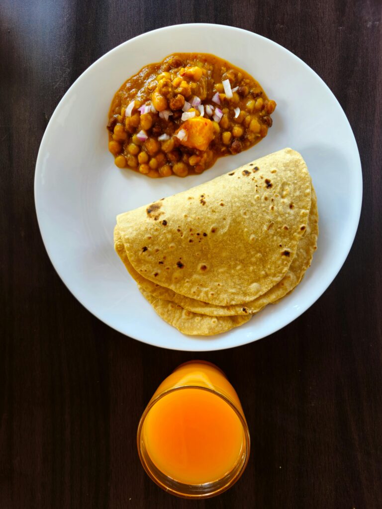 Overhead view of traditional Indian roti with chana masala and juice.