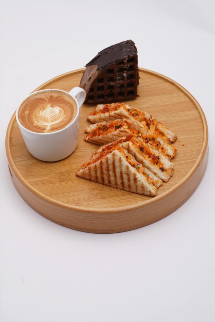 Artistic food presentation of coffee, sandwich and chocolate cake on a wooden platter.