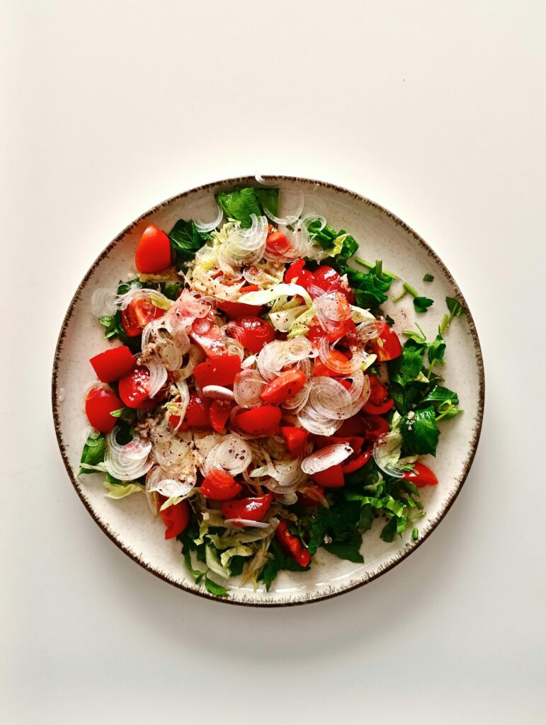 Colorful salad with cherry tomatoes, onions, and fresh greens in a white bowl.